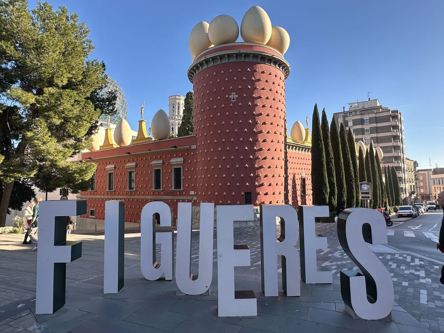 A red building with large white eggs on the roof, surrounded by trees and featuring large letters spelling "FIGUERES.