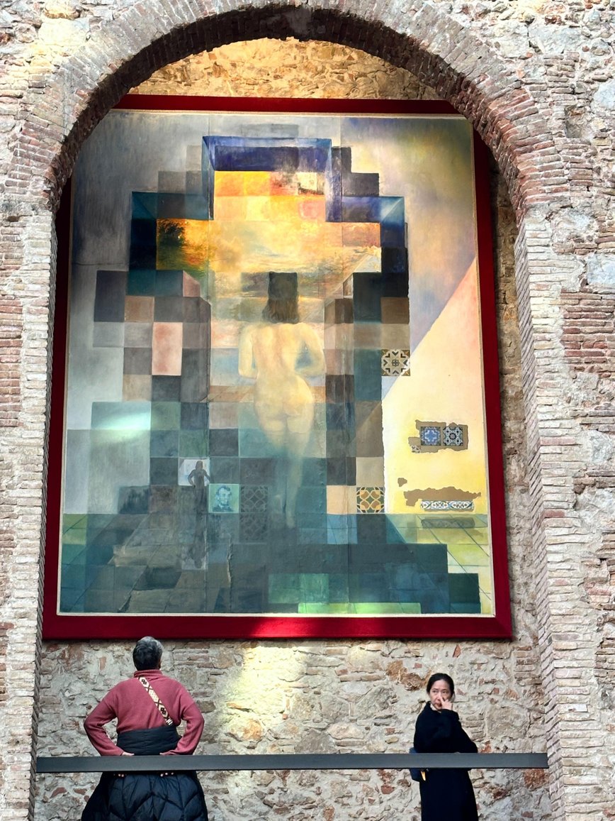 A cubist-style painting displayed on a brick wall with observers standing below.